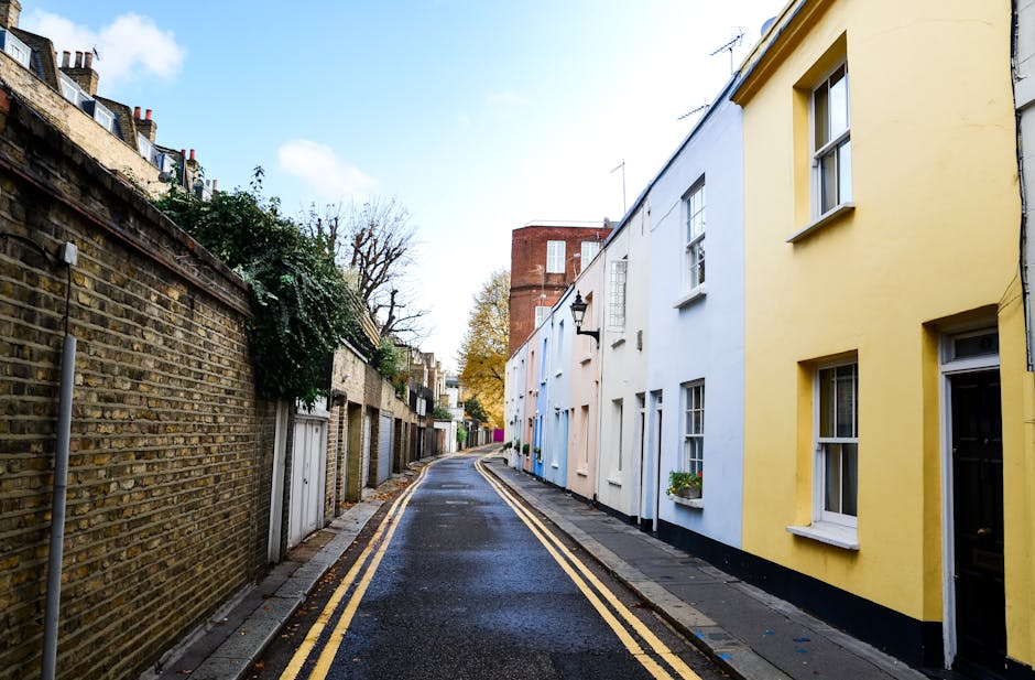 A narrow urban alleyway with weathered brick and corrugated metal walls, both covered in colourful graffiti tags and street art. The ground is uneven and muddy, with patches of wetness and scattered d